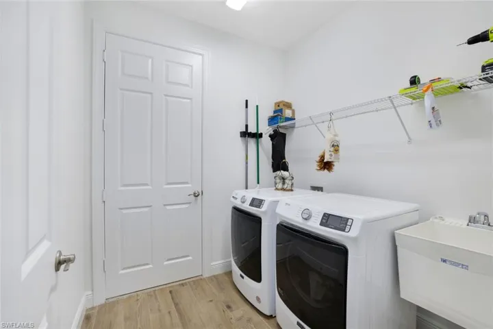 Clothes washing area featuring washing machine and dryer, light hardwood / wood-style flooring, and sink