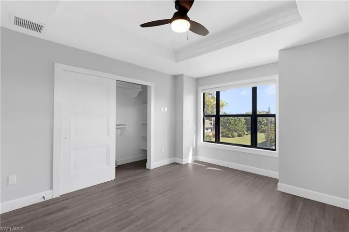 Unfurnished bedroom with ceiling fan, dark hardwood / wood-style floors, a closet, and a tray ceiling