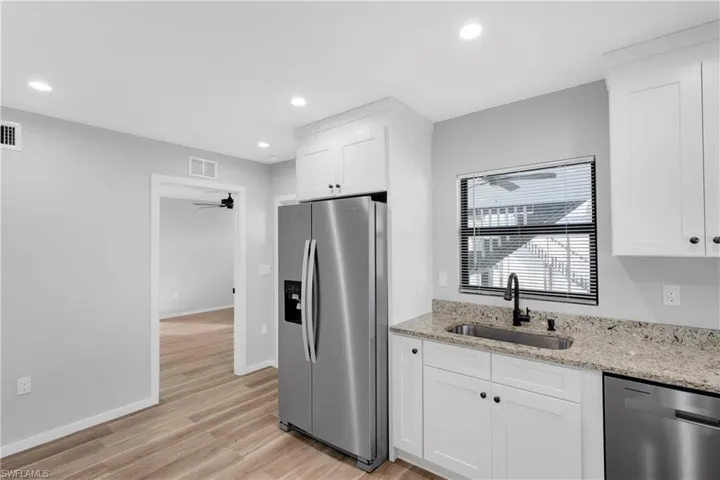 Kitchen featuring white cabinetry, sink, light stone counters, light hardwood / wood-style floors, and appliances with stainless steel finishes