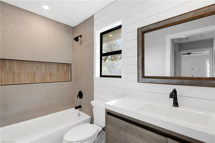 Full bathroom with vanity, wood walls, tiled shower / bath, ceiling fan, and toilet
