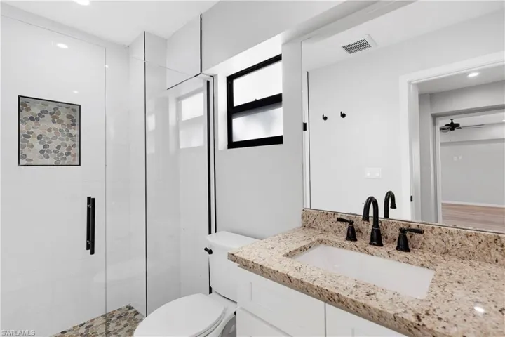 Bathroom featuring an enclosed shower, vanity, toilet, and ceiling fan