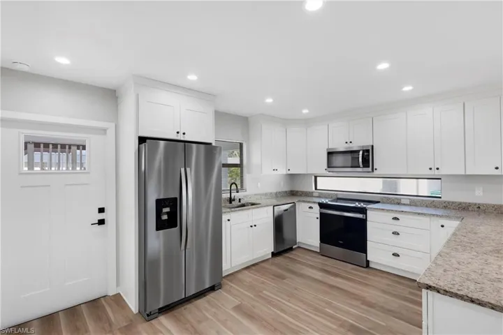 Kitchen featuring sink, stainless steel appliances, light stone counters, light hardwood / wood-style floors, and white cabinets
