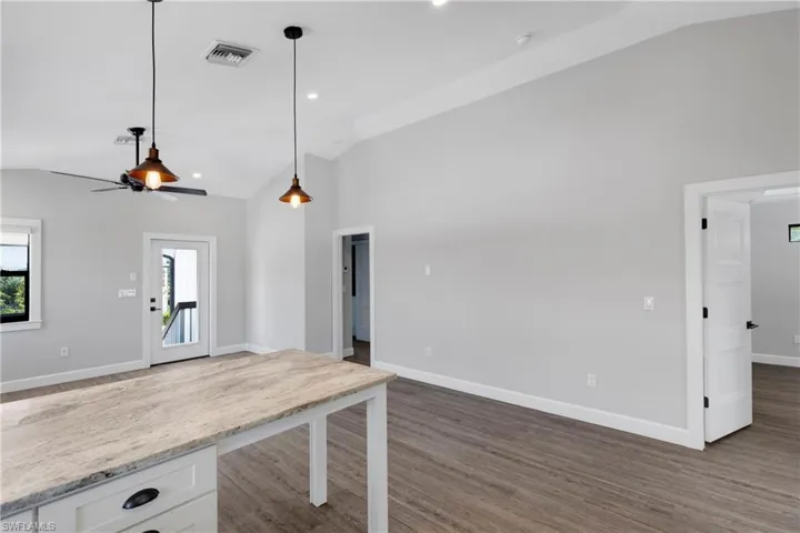 Kitchen with dark hardwood / wood-style floors, white cabinetry, decorative light fixtures, and vaulted ceiling