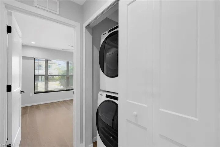 Washroom with wood-type flooring and stacked washer / dryer