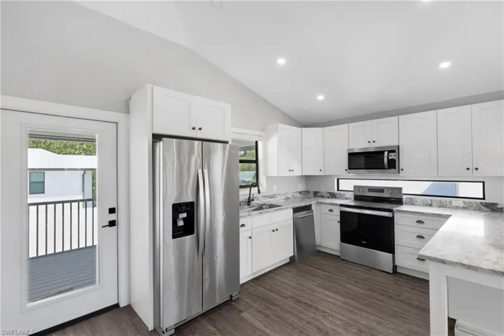 Kitchen with white cabinetry, dark hardwood / wood-style flooring, lofted ceiling, and appliances with stainless steel finishes