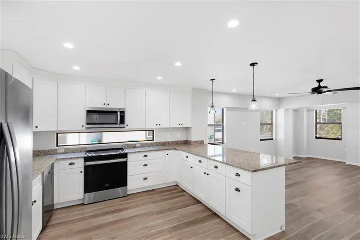 Kitchen featuring pendant lighting, kitchen peninsula, light wood-type flooring, appliances with stainless steel finishes, and white cabinetry