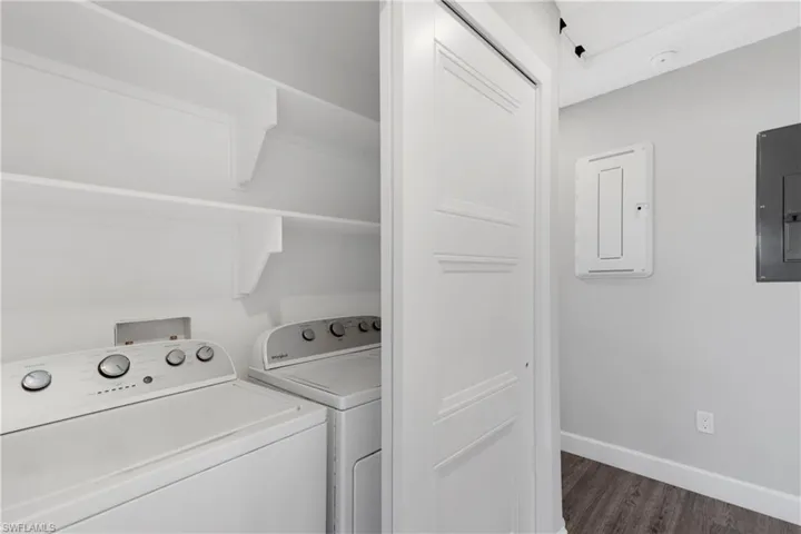Clothes washing area with washer and clothes dryer, dark hardwood / wood-style floors, and electric panel