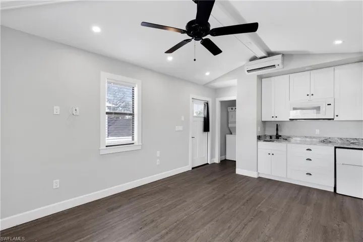 Kitchen featuring light stone countertops, dark hardwood / wood-style flooring, a wall unit AC, vaulted ceiling with beams, and white cabinetry