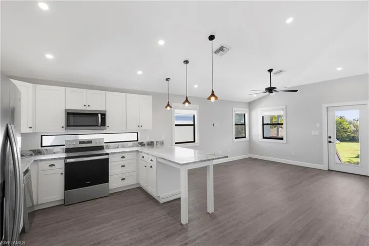Kitchen with kitchen peninsula, stainless steel appliances, white cabinets, dark hardwood / wood-style floors, and hanging light fixtures