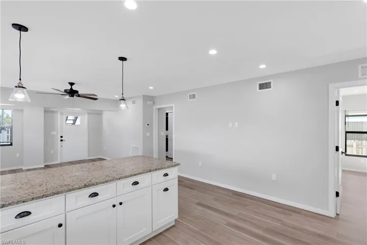 Kitchen with ceiling fan, light stone counters, light hardwood / wood-style flooring, pendant lighting, and white cabinets