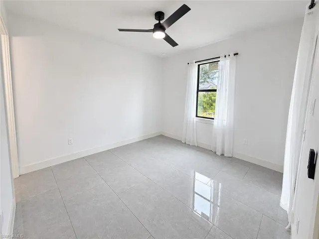 Neutral-toned interior space featuring high-gloss tile flooring, a matte black ceiling fan with integrated lighting, and a window with a black frame