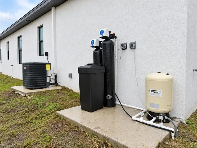Exterior wall-mounted central air conditioning unit and water treatment system featuring a pressure tank and filtration tanks on concrete pads