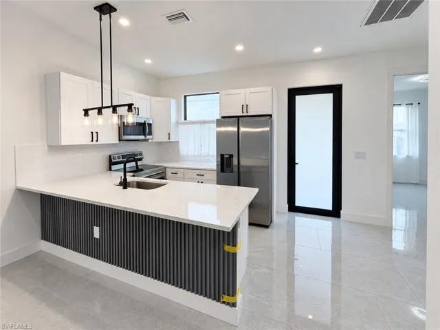Kitchen featuring white shaker-style cabinetry, quartz countertops, a slatted charcoal accent island, stainless steel appliances, and tile flooring