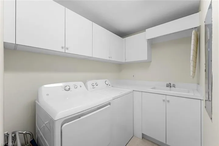 Laundry area with cabinets, light tile patterned floors, washer and clothes dryer, and sink