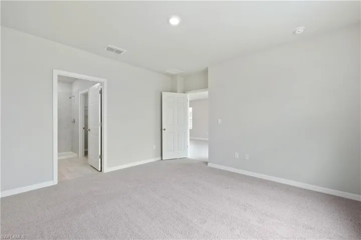 Unfurnished bedroom with ensuite bathroom and light carpet