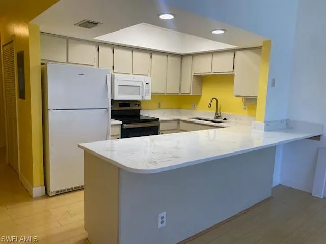 Kitchen featuring white appliances, a peninsula, recessed lighting, light wood-style flooring, and light stone counters