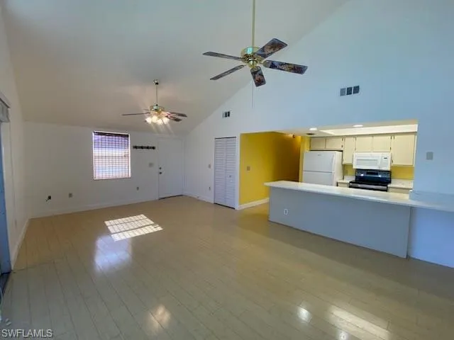 Unfurnished living room with high vaulted ceiling, light wood-type flooring, and a ceiling fan