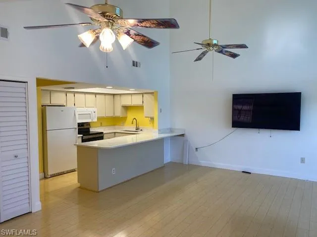 Kitchen featuring a towering ceiling, white appliances, a peninsula, ceiling fan, and light wood-style flooring