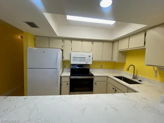 Kitchen featuring white appliances, light stone counters, a raised ceiling, and cream cabinetry