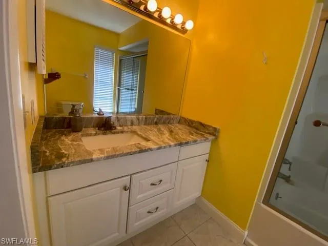 Bathroom with vanity, bath / shower combo with glass door, and light tile patterned floors