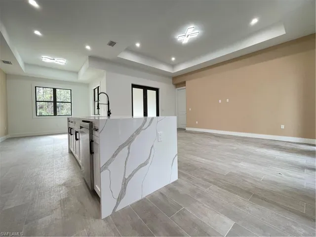 Kitchen featuring sink, light stone counters, a center island with sink, a tray ceiling, and white cabinets