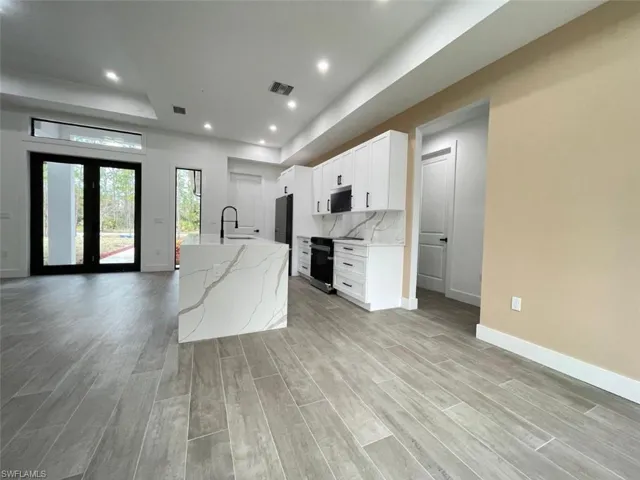 Kitchen with white cabinetry, light stone counters, a center island with sink, light hardwood / wood-style floors, and backsplash