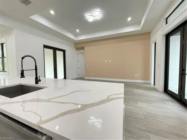 Kitchen with a tray ceiling, light stone countertops, sink, and french doors