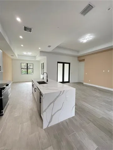 Kitchen featuring sink, white cabinetry, a kitchen island with sink, light stone counters, and a raised ceiling