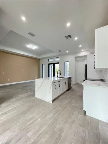 Kitchen with white cabinetry, an island with sink, sink, light stone counters, and a tray ceiling
