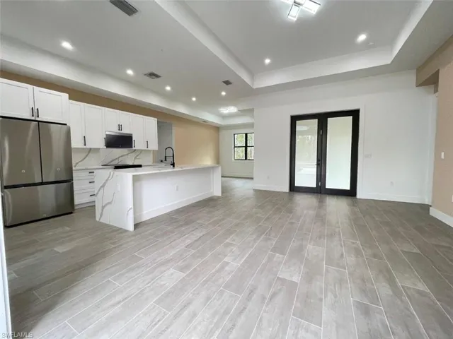 Kitchen featuring appliances with stainless steel finishes, a raised ceiling, a center island with sink, and white cabinets