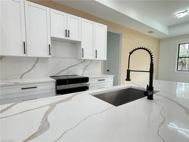 Kitchen featuring white cabinetry, sink, light stone counters, and stainless steel electric range
