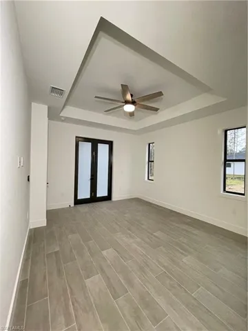 Unfurnished room featuring a raised ceiling, hardwood / wood-style flooring, ceiling fan, and french doors