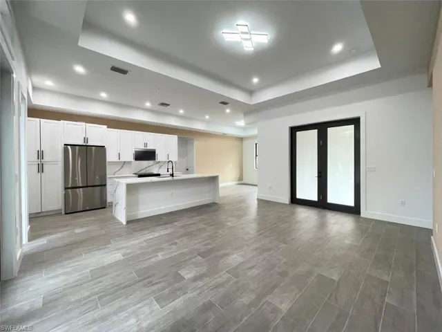 Kitchen with white cabinetry, appliances with stainless steel finishes, a tray ceiling, and a kitchen island with sink