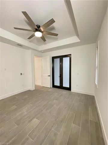 Spare room featuring hardwood / wood-style floors, a tray ceiling, french doors, and ceiling fan