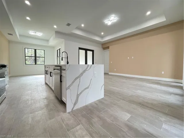 Kitchen featuring dishwasher, light stone counters, an island with sink, white cabinets, and a raised ceiling