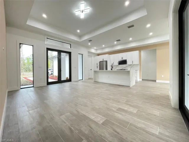 Unfurnished living room with a raised ceiling, sink, light hardwood / wood-style flooring, and french doors