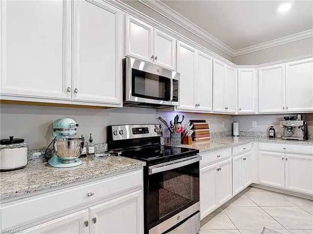 Kitchen with white cabinets, appliances with stainless steel finishes, light stone counters, and crown molding