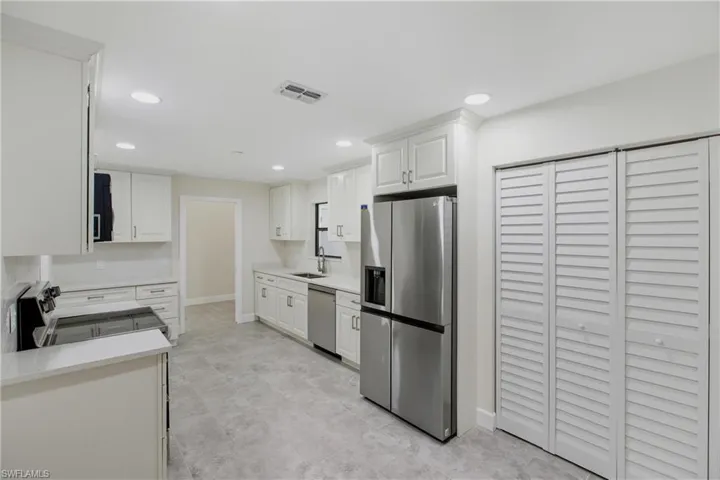 Kitchen with stainless steel appliances, white cabinets, recessed lighting, and light stone countertops