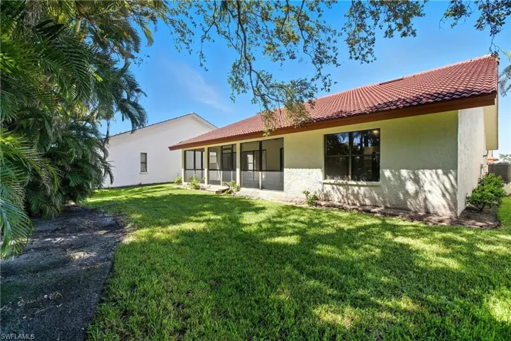Rear view of property featuring a sunroom, stucco siding, a yard, and a tiled roof