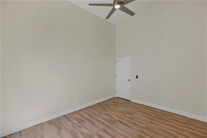Empty room with light wood-style floors, high vaulted ceiling, and ceiling fan