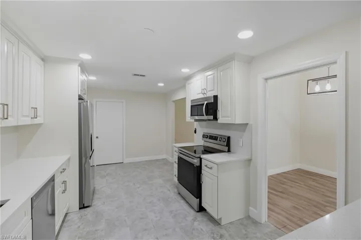 Kitchen with appliances with stainless steel finishes, white cabinets, light stone counters, and recessed lighting