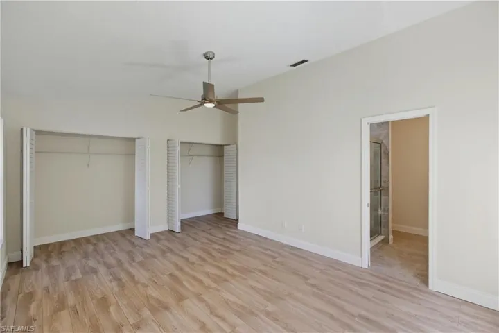 Unfurnished bedroom with two closets, light wood-style flooring, a ceiling fan, and lofted ceiling
