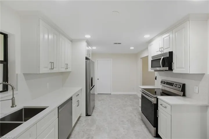 Kitchen with appliances with stainless steel finishes, white cabinets, light stone counters, and recessed lighting