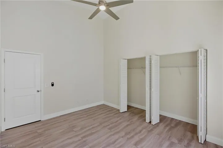 Unfurnished bedroom with a high ceiling, light wood-style floors, multiple closets, and a ceiling fan