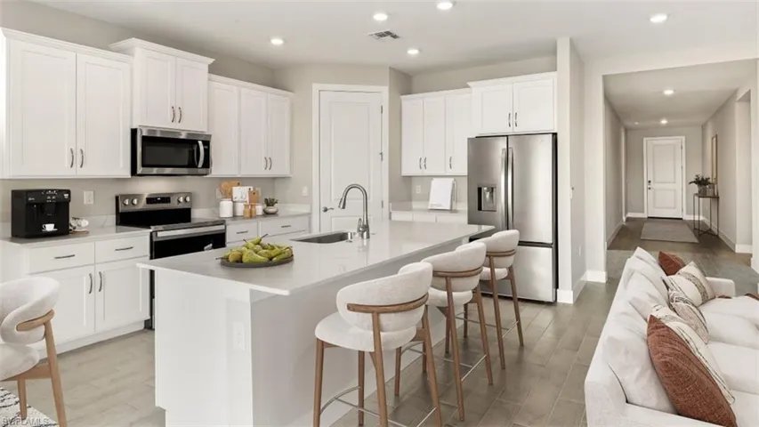 Kitchen featuring white shaker cabinetry, stainless steel appliances, a center island with countertop seating, and wood-finish flooring