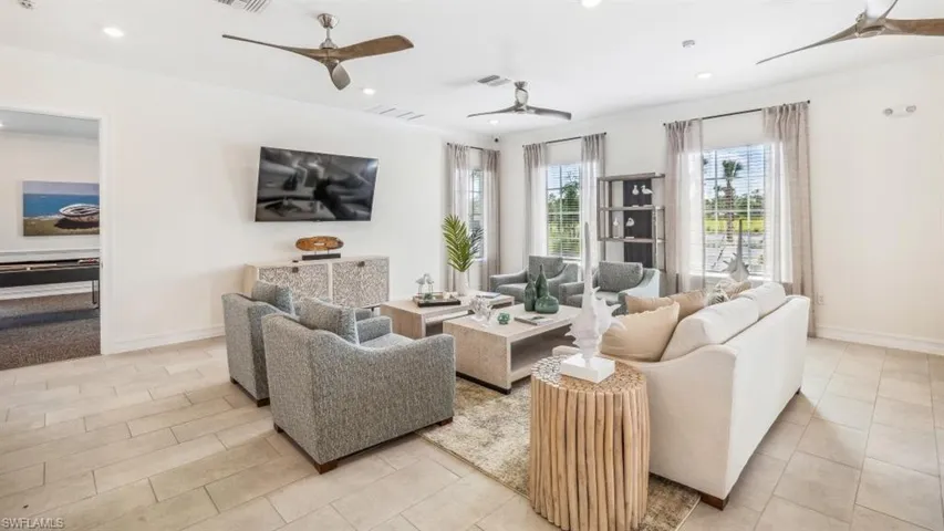 Spacious living area featuring light-toned tile flooring, multiple windows providing ample natural light, and recessed lighting with ceiling fans