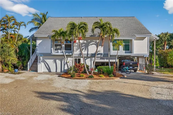 Coastal home featuring stairway, gravel driveway, roof with shingles, a carport, and a garage