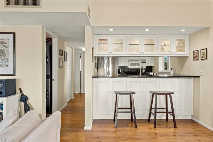 Kitchen featuring white cabinetry, glass insert cabinets, a kitchen breakfast bar, stainless steel fridge, and light wood-type flooring