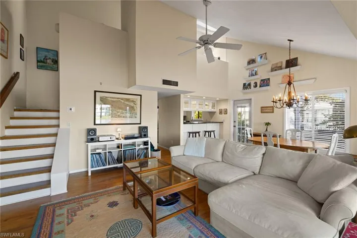 Living room with dark wood-style floors, stairs, high vaulted ceiling, a chandelier, and a ceiling fan