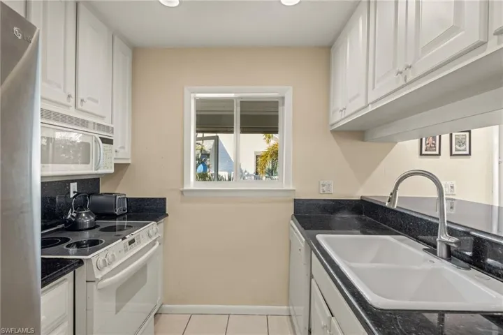 Kitchen with white appliances, white cabinetry, light tile patterned floors, recessed lighting, and dark stone counters